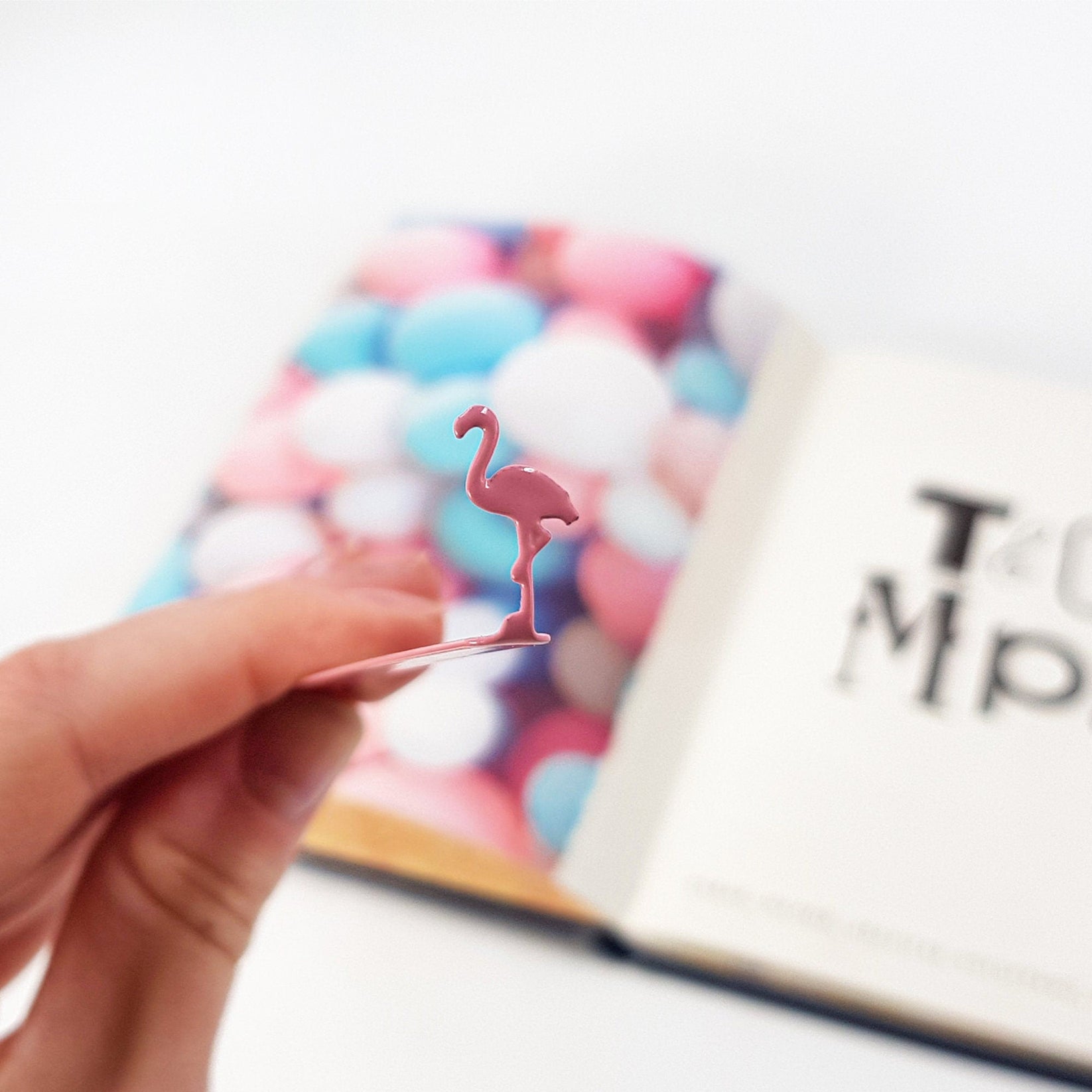 Flamingo metal bookmark in red held in a hand above an open book