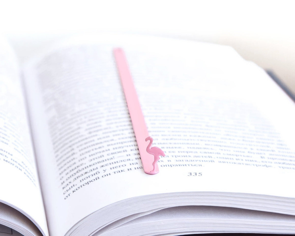 Flamingo metal bookmark in red lying across the pages of an open book