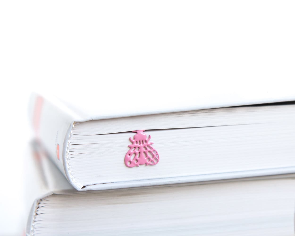 Fly metal bookmark in red in a closed book, only its top showing above the pages