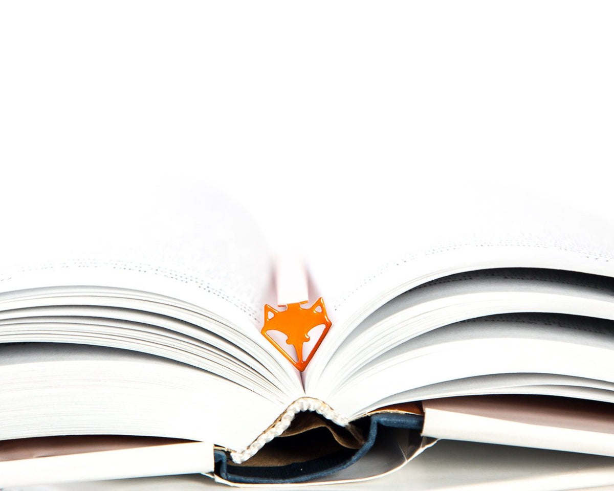 Fox Head metal bookmark in red marking a page in an open book