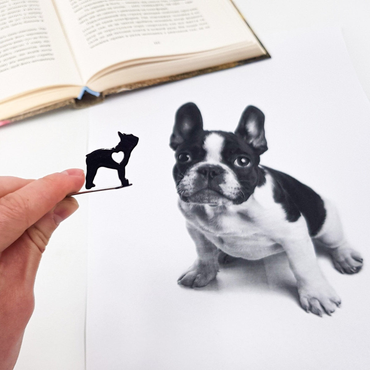 French Bulldog Love metal bookmark held in a hand above an open book
