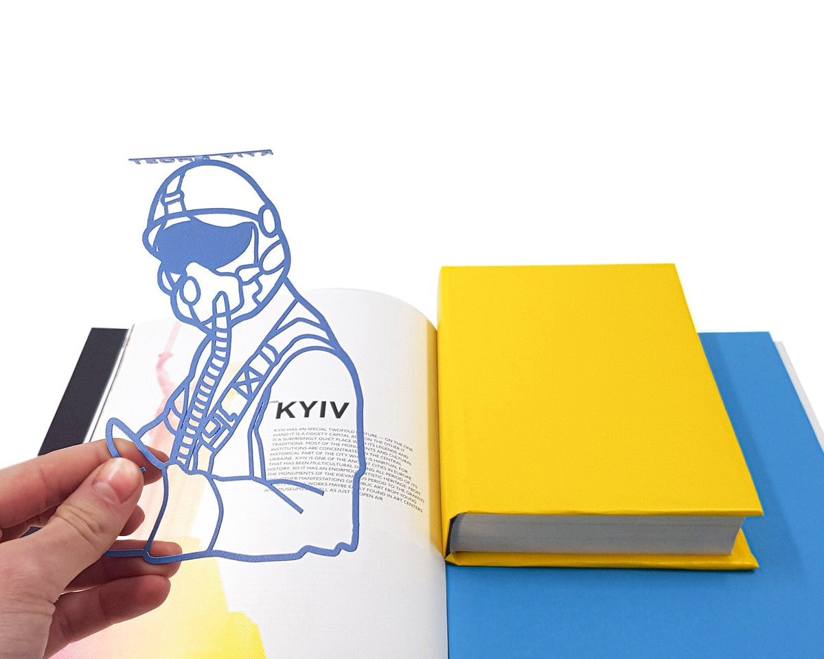 Ghost of Kyiv metal bookmark held in a hand above an open book