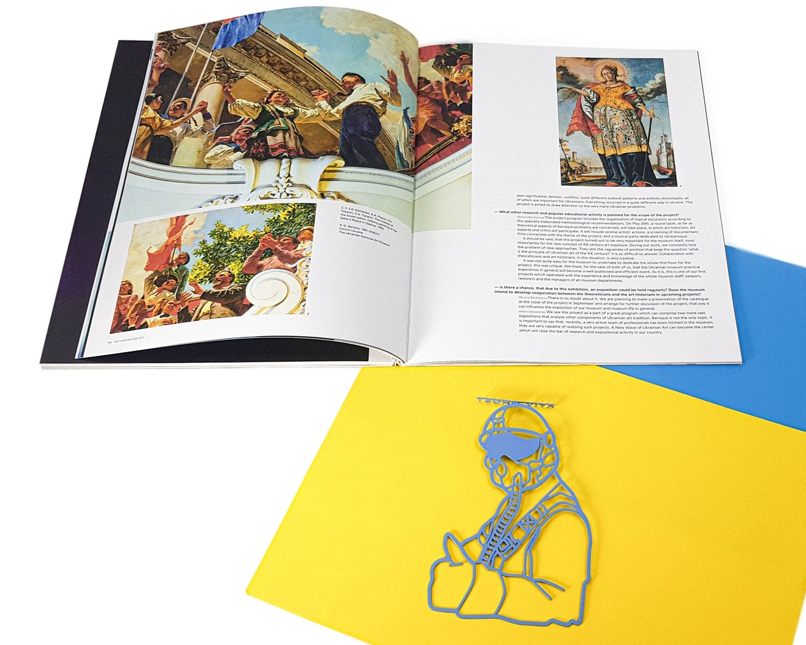 Ghost of Kyiv metal bookmark placed on a colour illustration