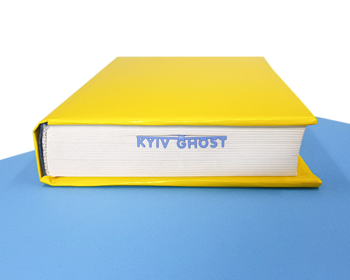 Ghost of Kyiv metal bookmark in blue in a closed book, only its top showing above the pages
