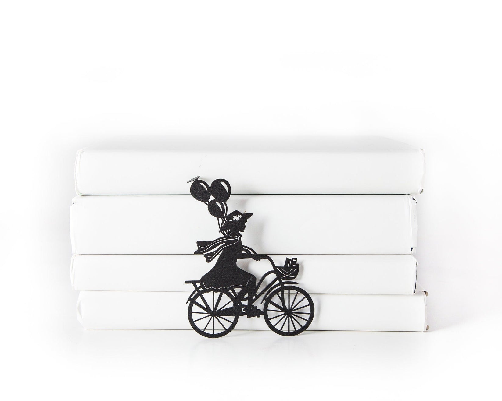 Girl on the Bike with Balloons metal bookmark shown with a stack of books