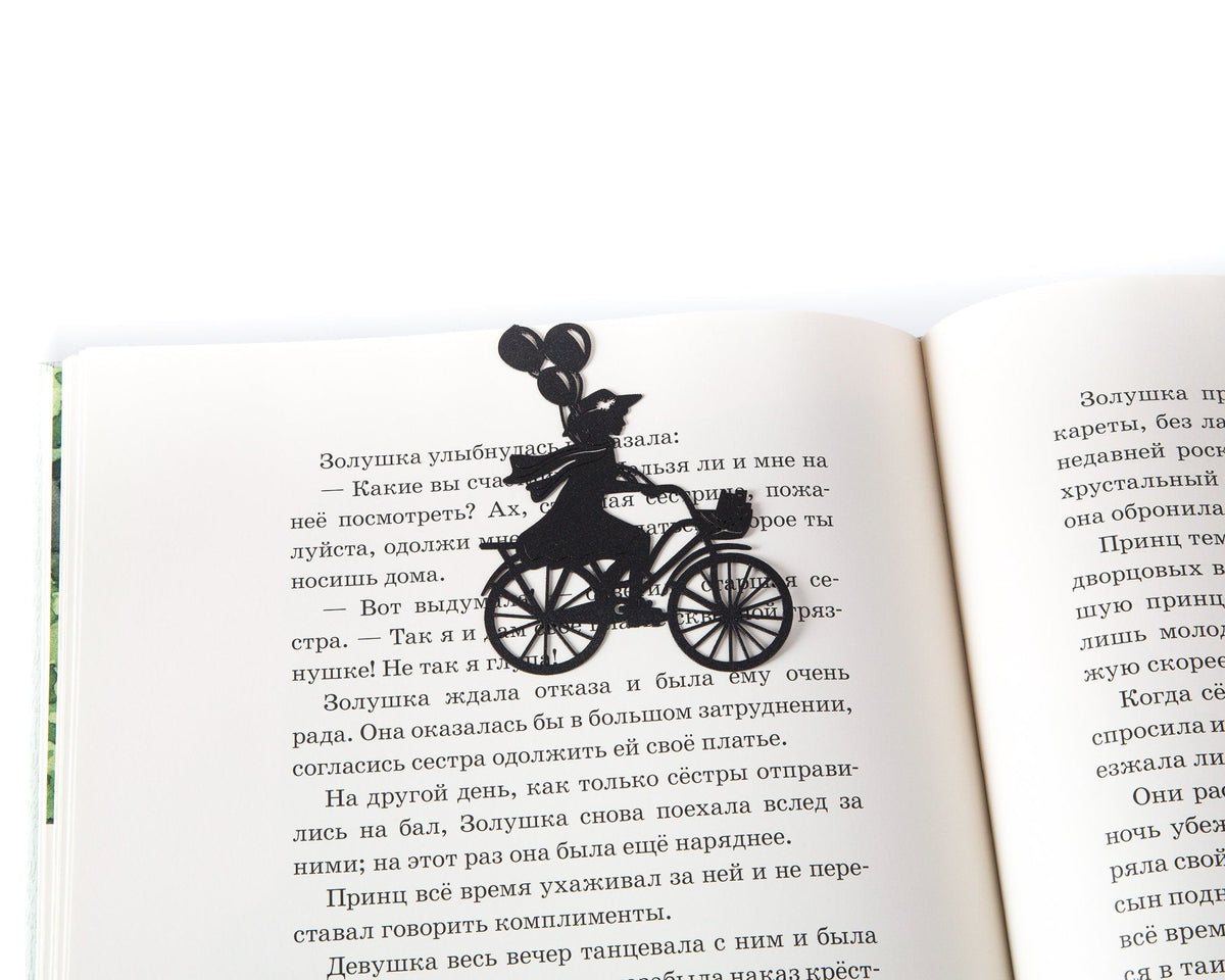 Girl on the Bike with Balloons metal bookmark resting on the pages of an open book