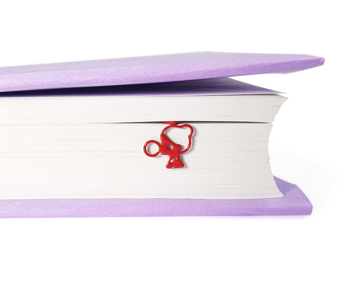 Girl with a Bubble Gum metal bookmark in red in a closed book, only its top showing above the pages