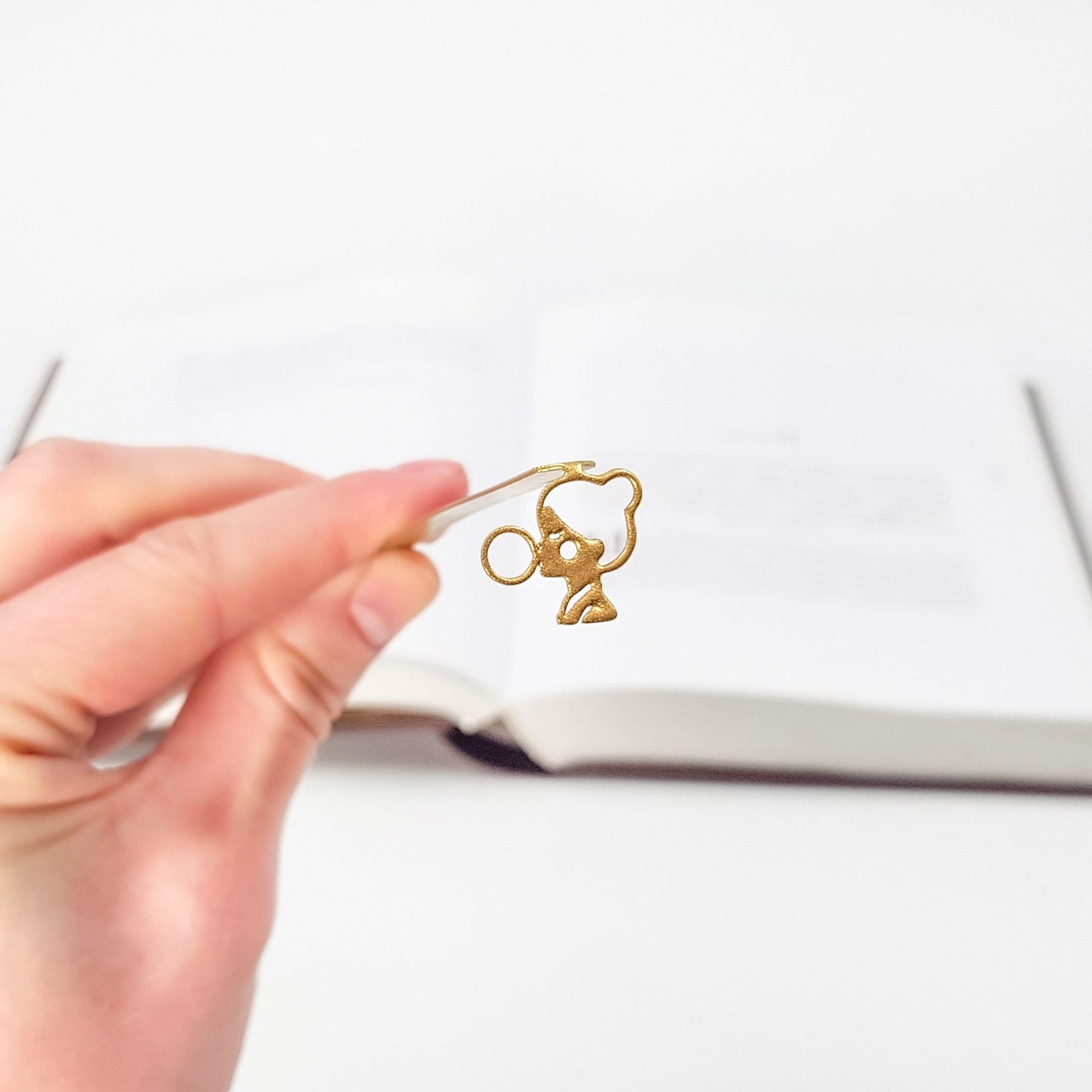Girl with a Bubble Gum metal bookmark in gold held in a hand above an open book