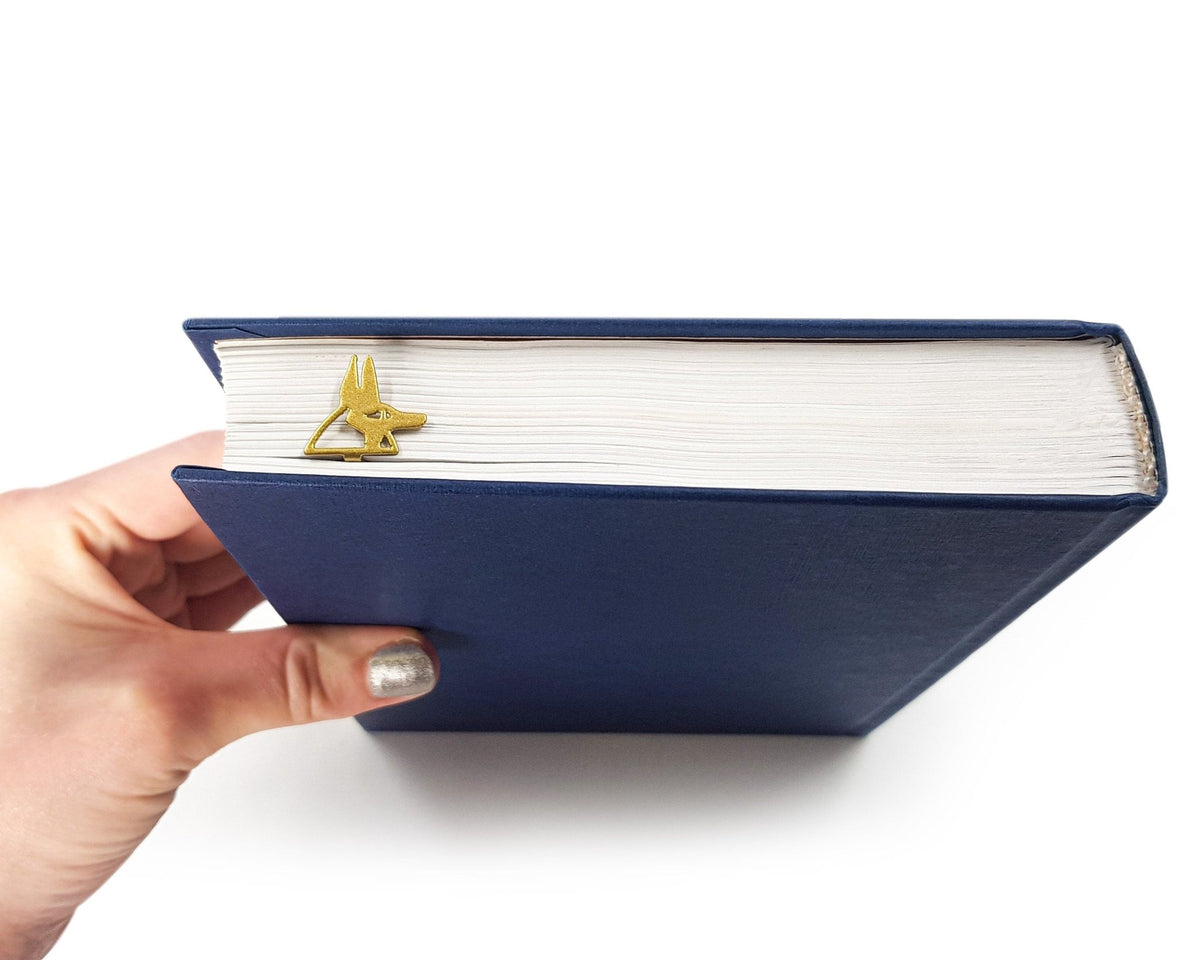 God of Death Anubis metal bookmark in gold held in a hand above an open book