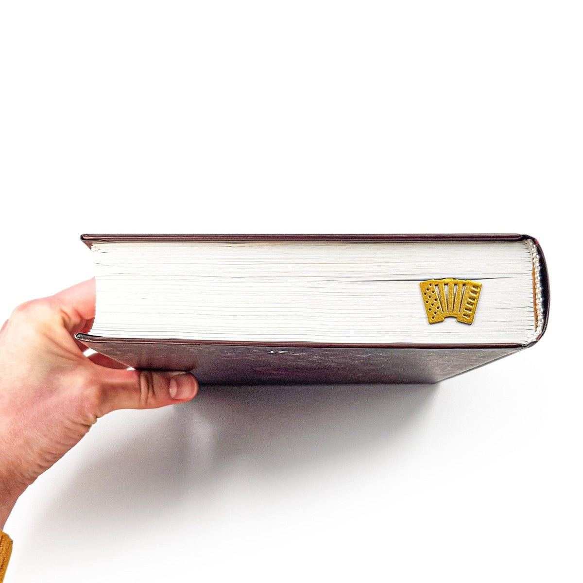 Golden Accordion metal bookmark in gold held up beside an open book