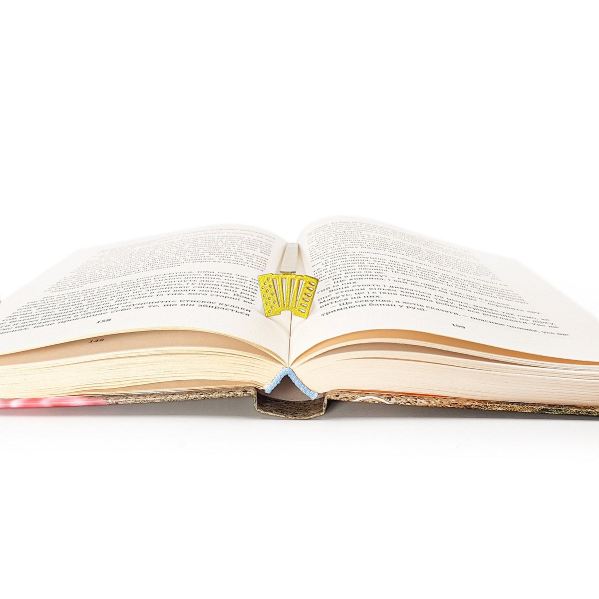Golden Accordion metal bookmark in gold lying across the pages of an open book