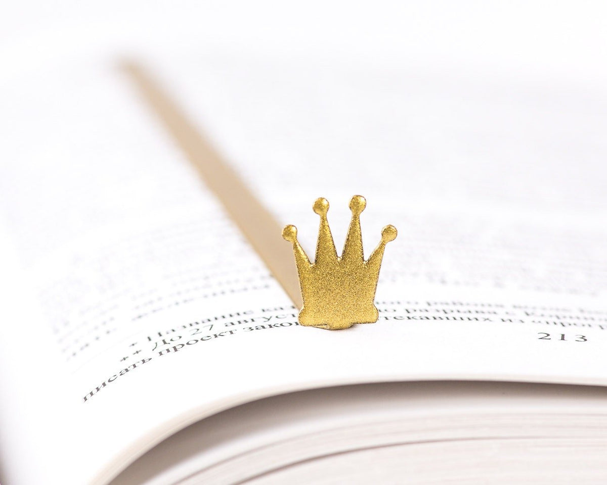 Golden Crown metal bookmark in gold resting on the pages of an open book
