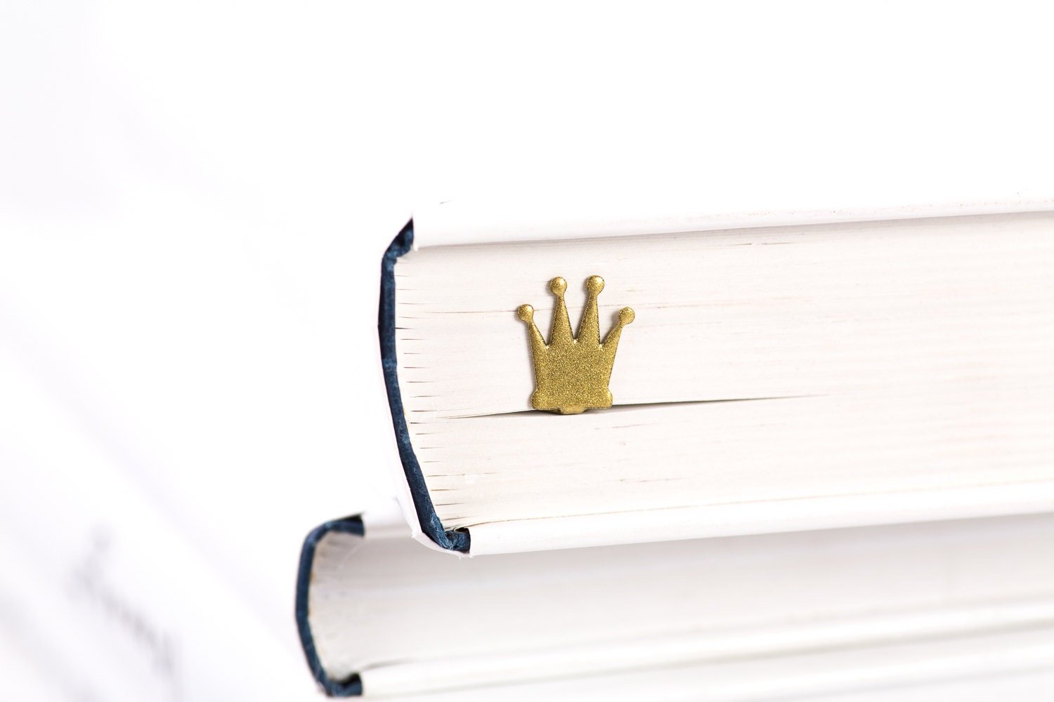 Golden Crown metal bookmark in gold in a closed book, only its top showing above the pages
