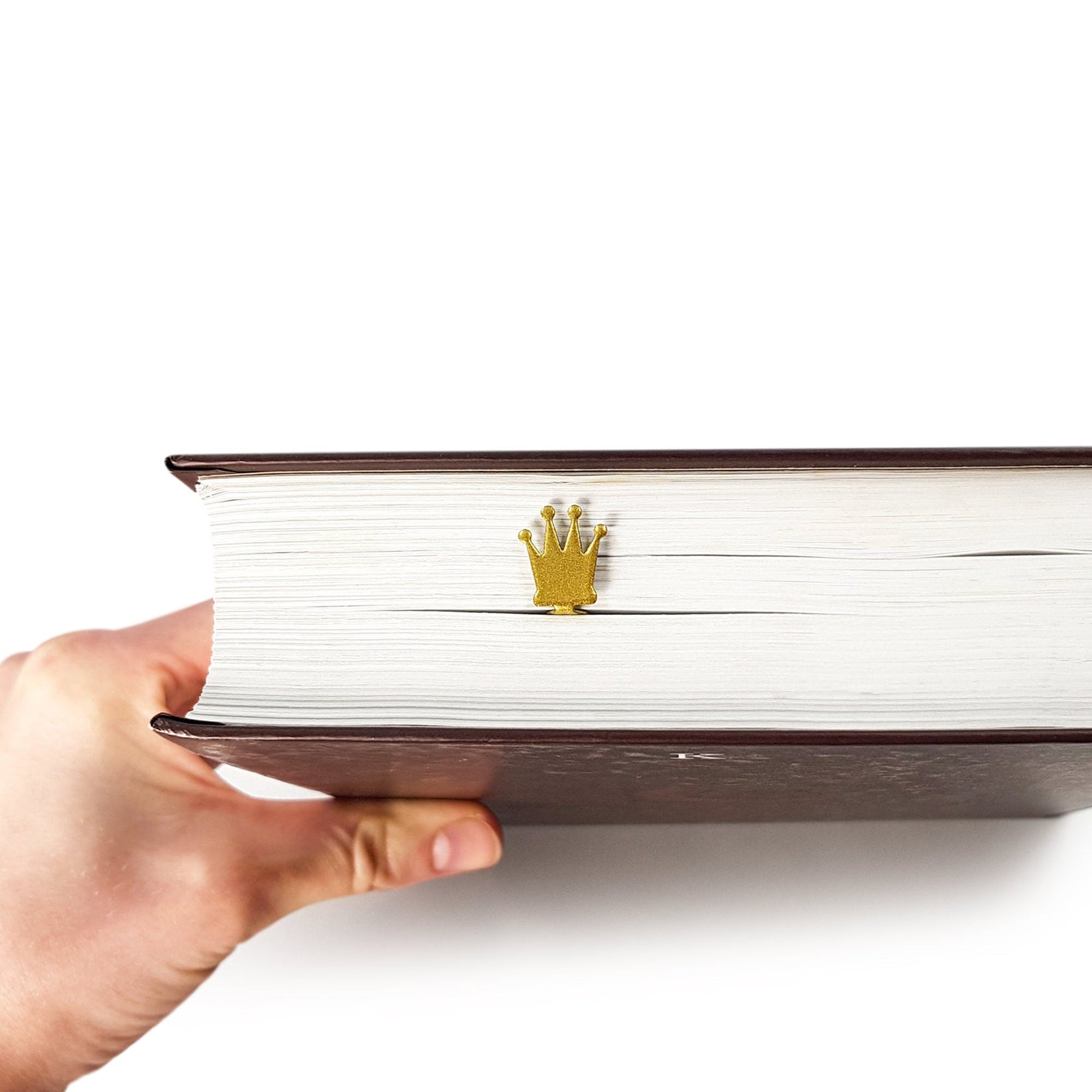 Golden Crown metal bookmark in gold held in a hand above an open book
