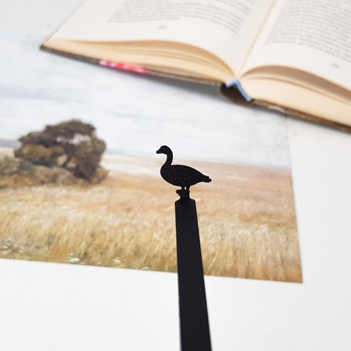 Goose metal bookmark marking a page in an illustrated book
