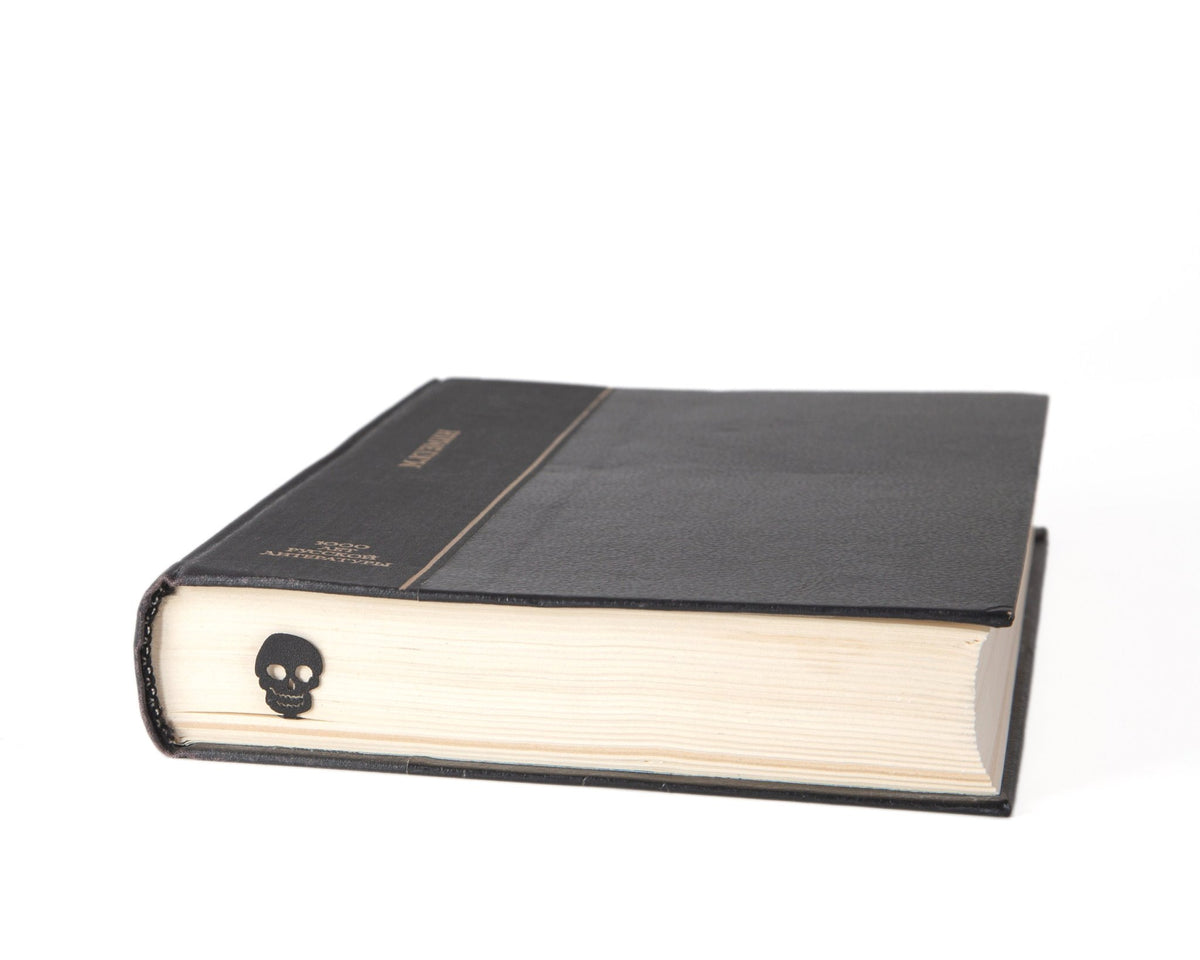 Grinning Skull metal bookmark in a closed book, only its top showing above the pages