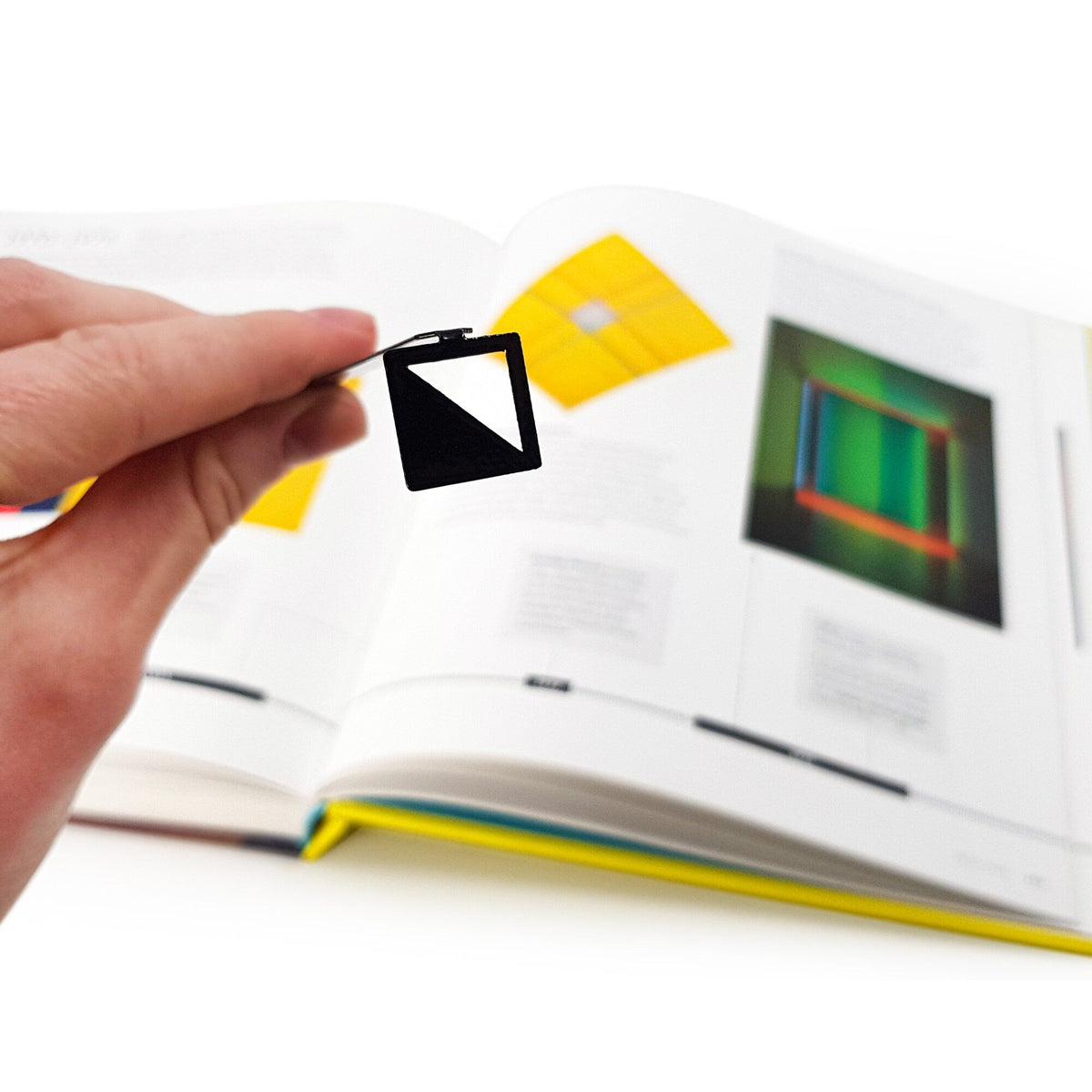 Half Square metal bookmark held in a hand above an open book