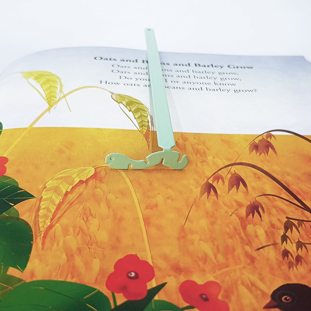Happy metal bookmark in green marking a page in an illustrated book, view 4