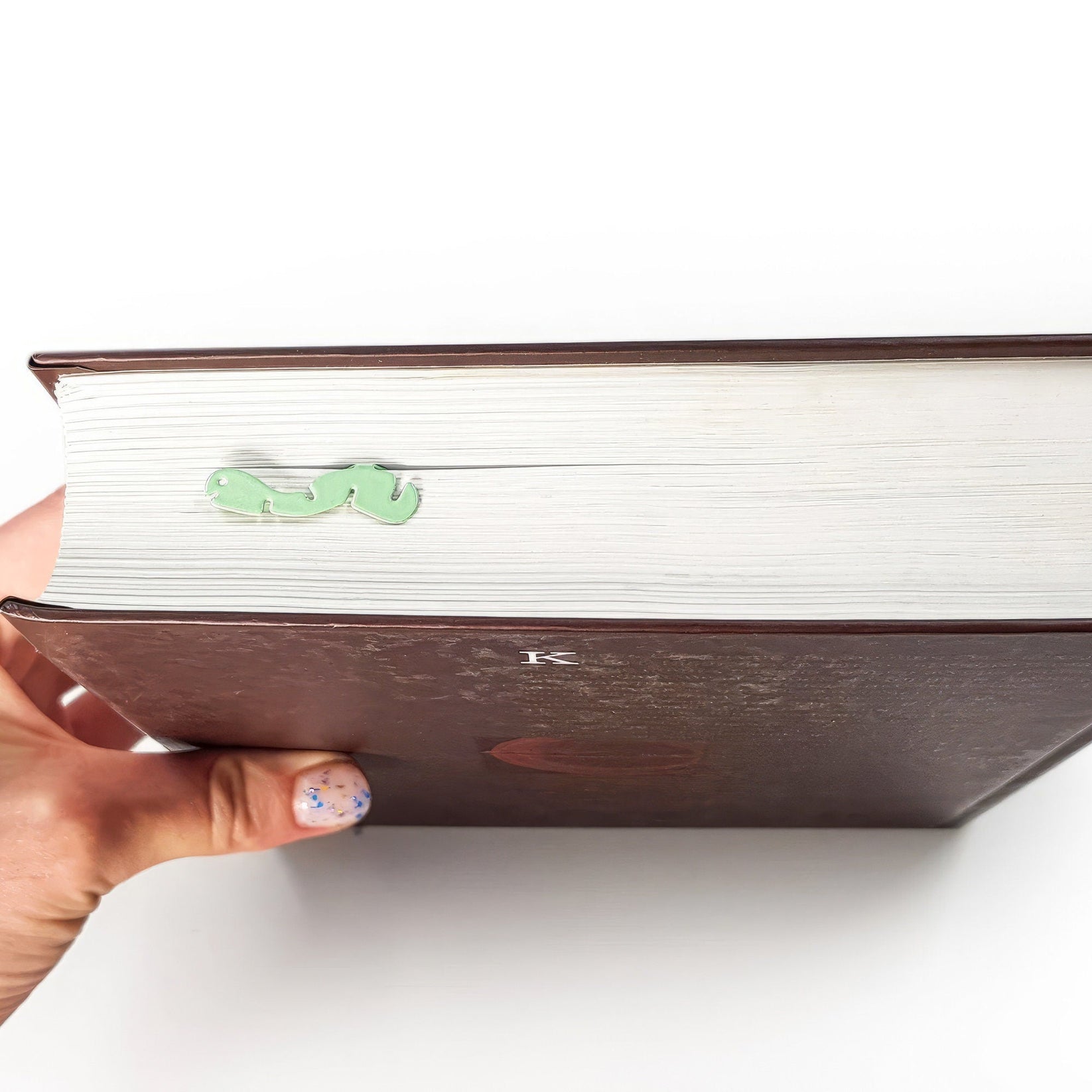 Happy metal bookmark in green held in a hand above an open book