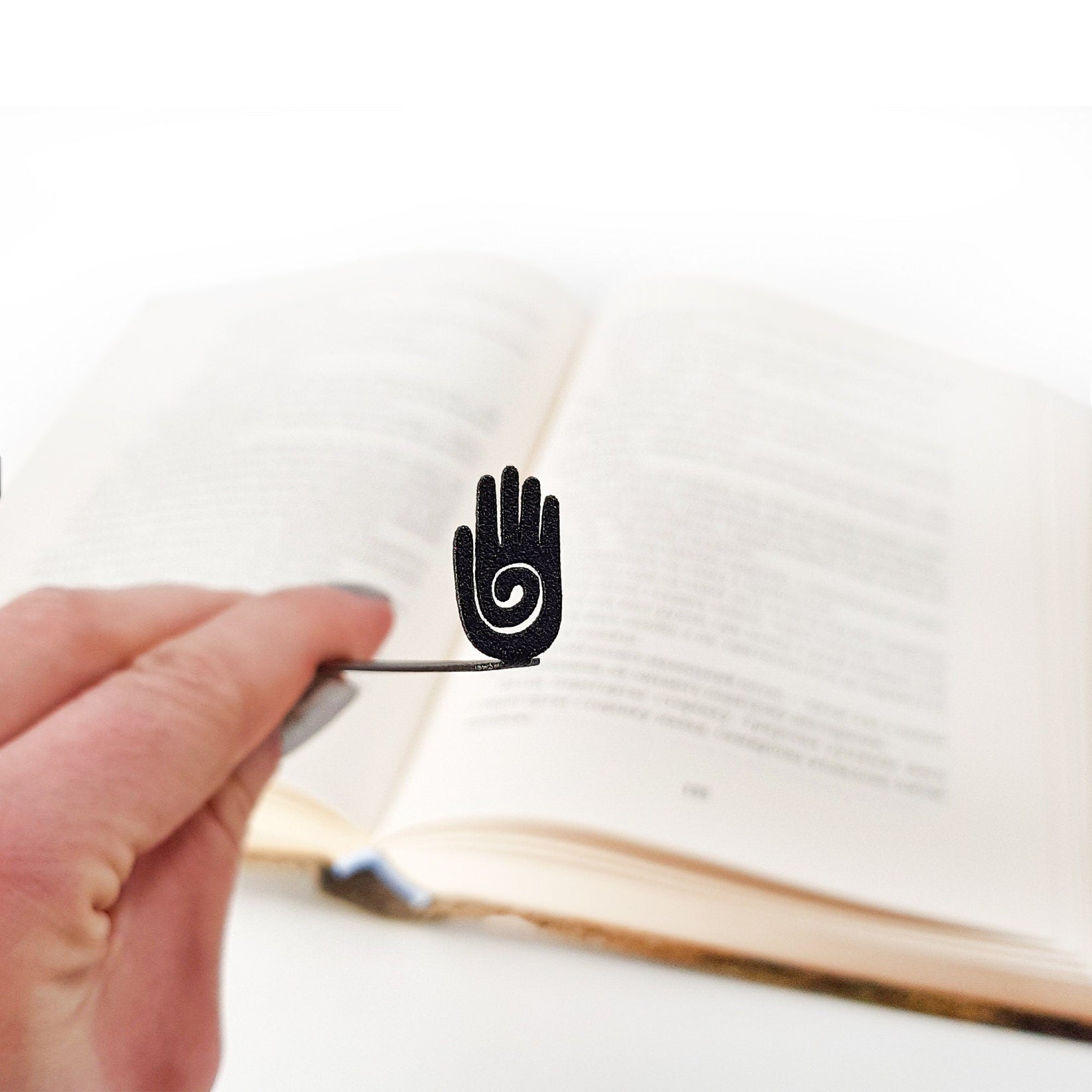 Healing Hand metal bookmark held in a hand above an open book