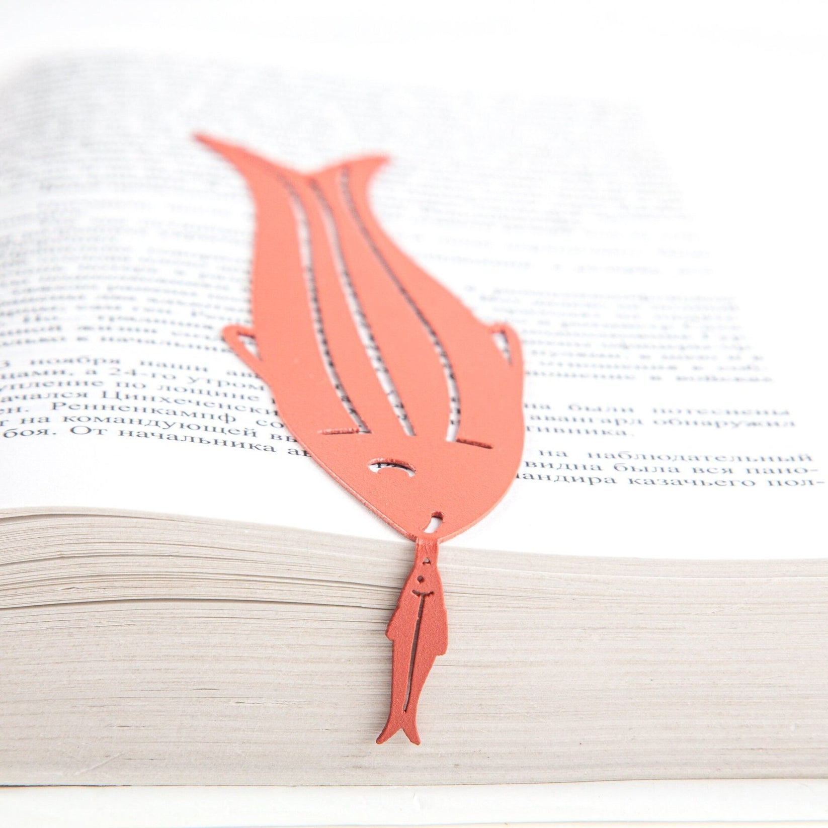 Herring metal bookmark in red lying across the pages of an open book