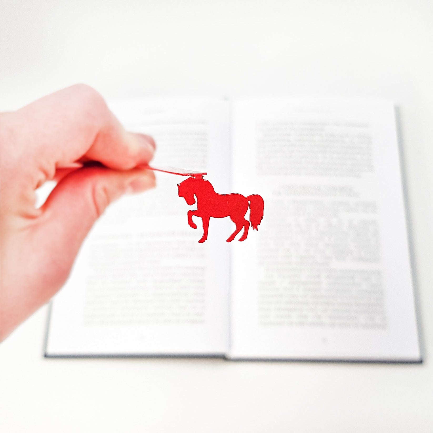 Horse metal bookmark in red held in a hand above an open book
