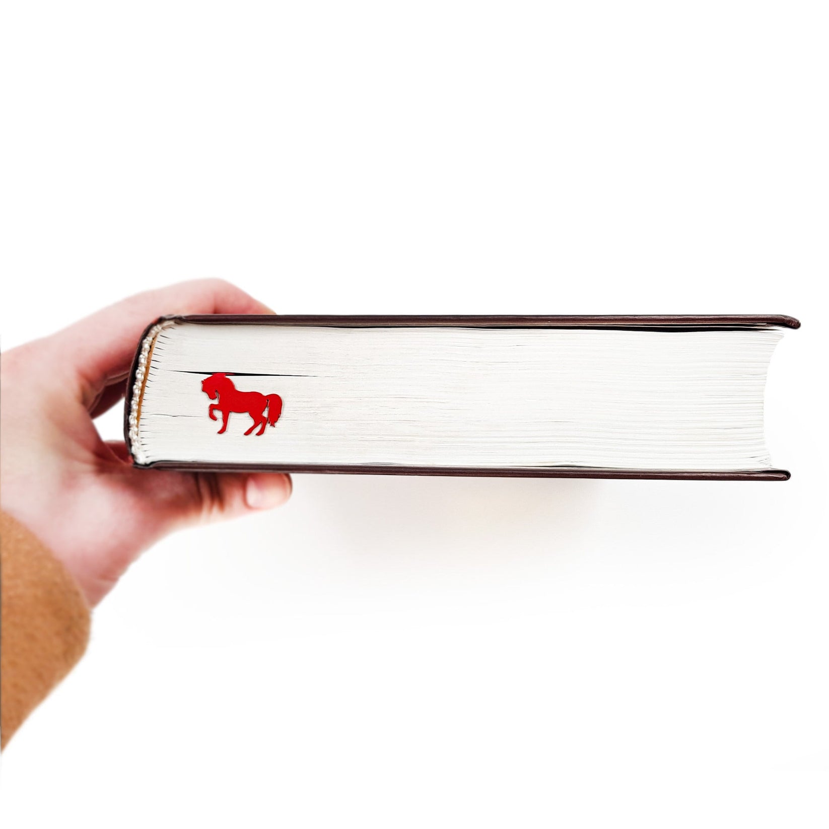 Horse metal bookmark in red held up beside an open book