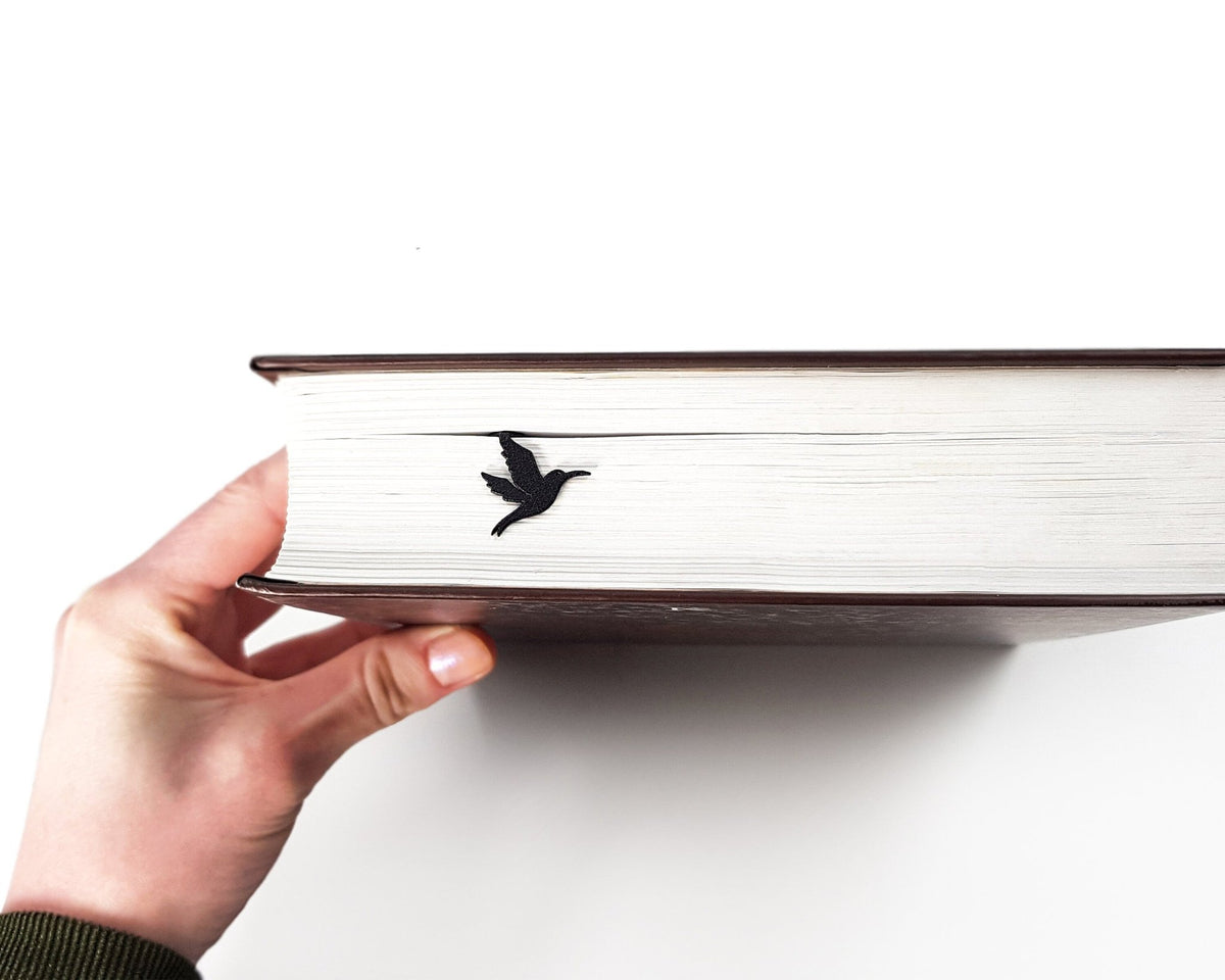 Hummingbird metal bookmark held in a hand above an open book