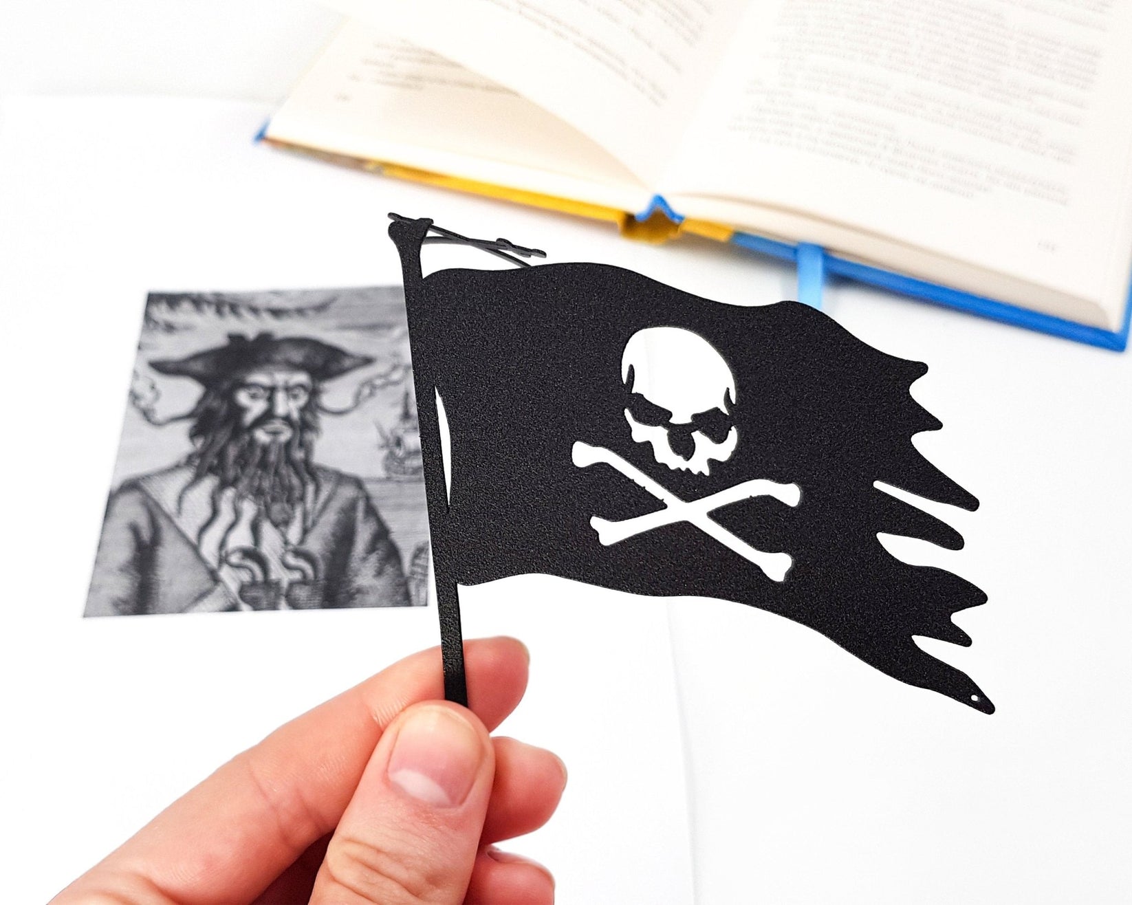 Jolly Rogers metal bookmark held in a hand above an open book