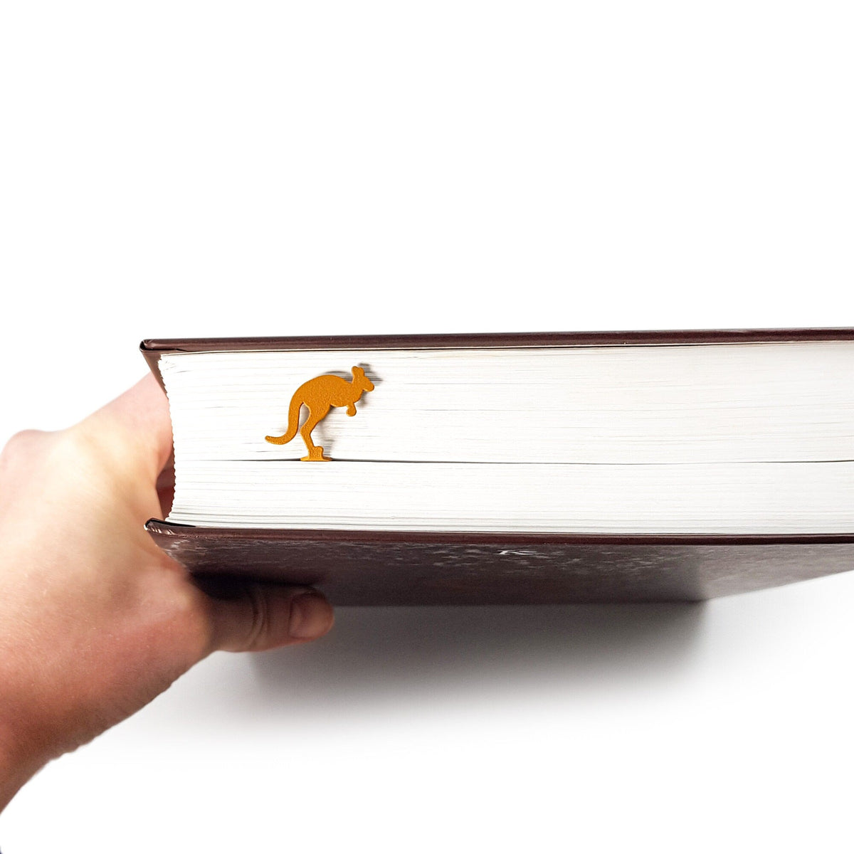 Kangaroo metal bookmark in gold held in a hand above an open book