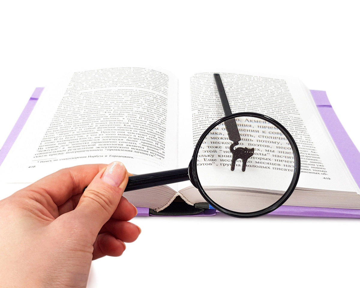 Kitty Grace metal bookmark held in a hand above an open book