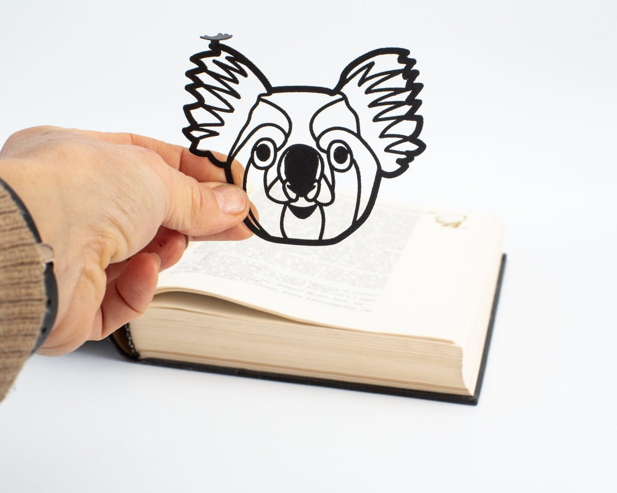 Koala metal bookmark held in a hand above an open book