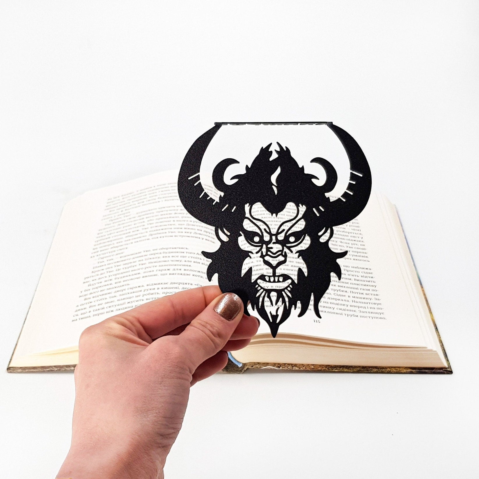 Krampus metal bookmark held in a hand above an open book