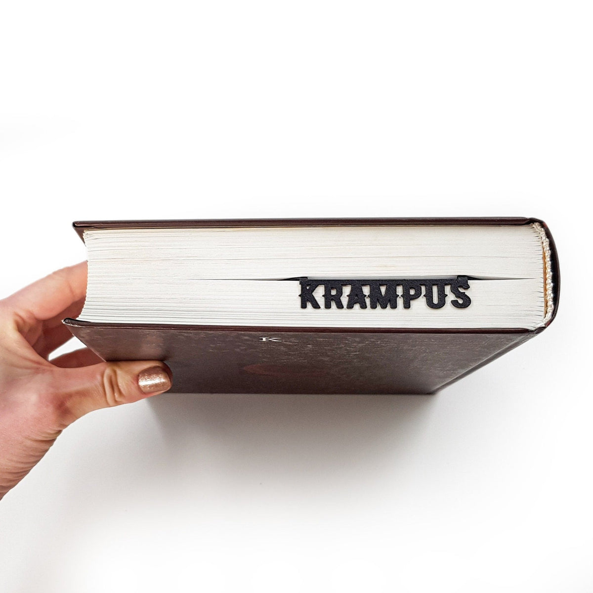 Krampus metal bookmark held up beside an open book