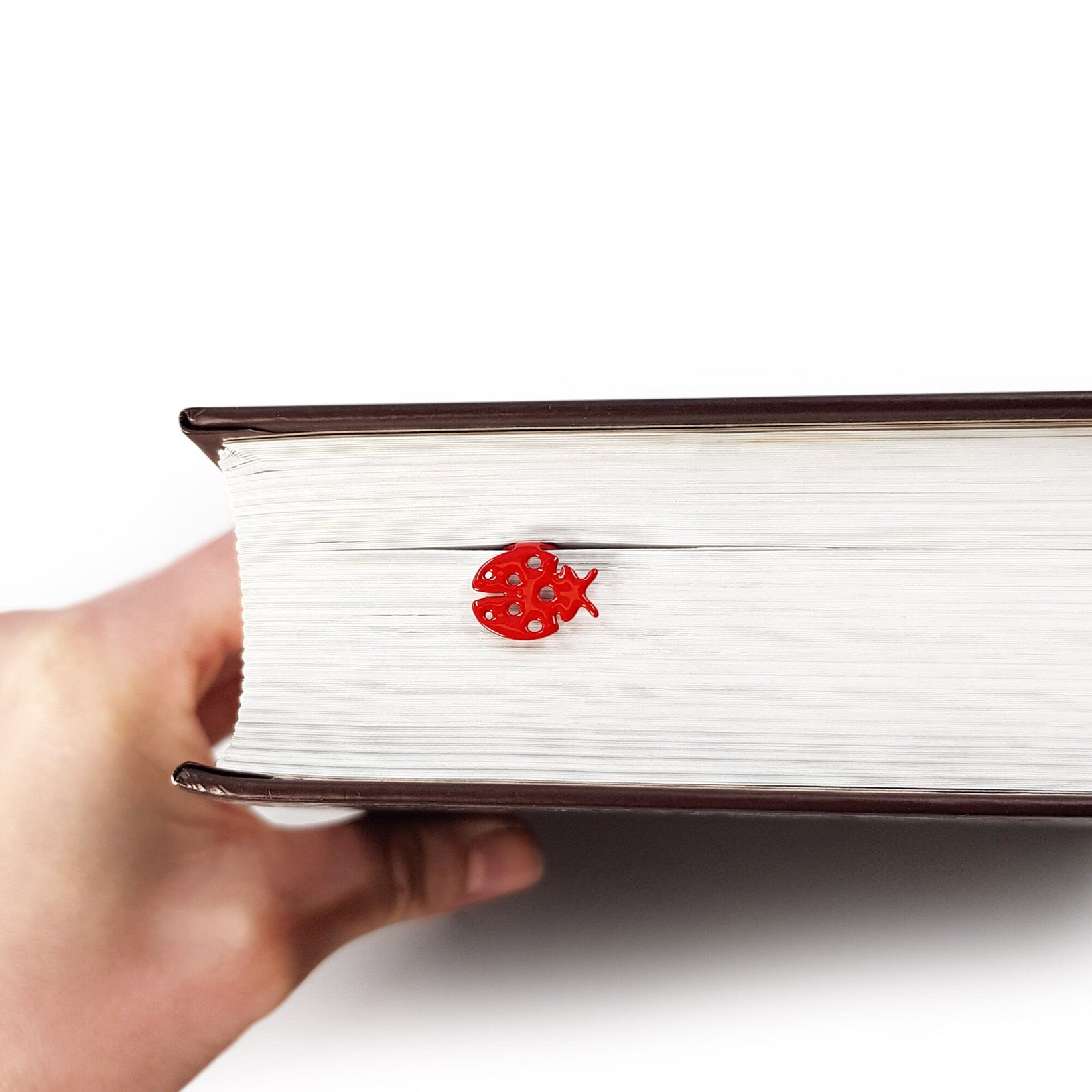 Ladybird metal bookmark in red held in a hand above an open book