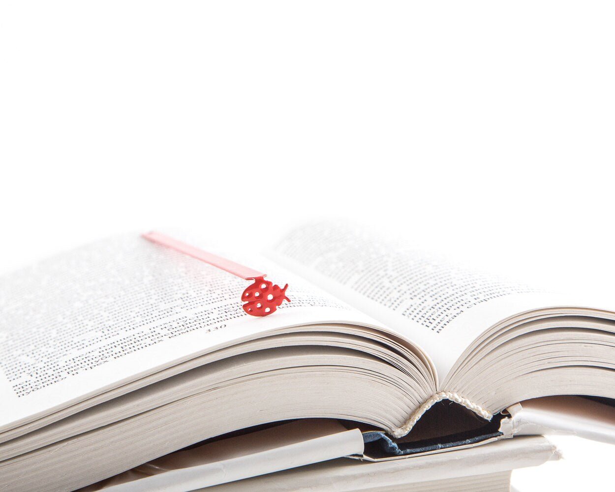 Ladybird metal bookmark in red resting on the pages of an open book