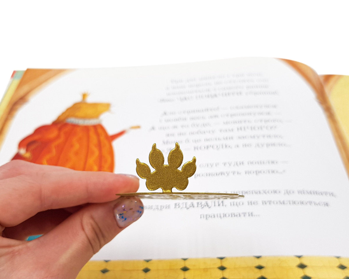 Lion Head metal bookmark in gold placed on a colour illustration
