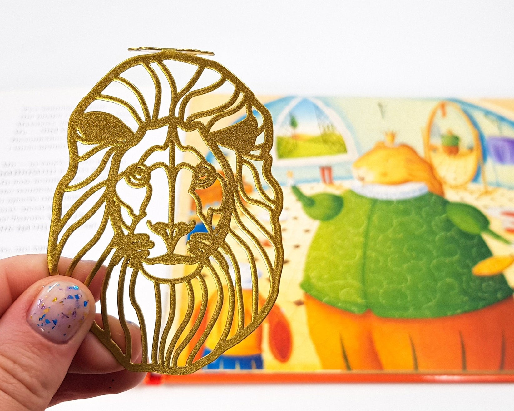 Lion Head metal bookmark in gold marking a page in an illustrated book