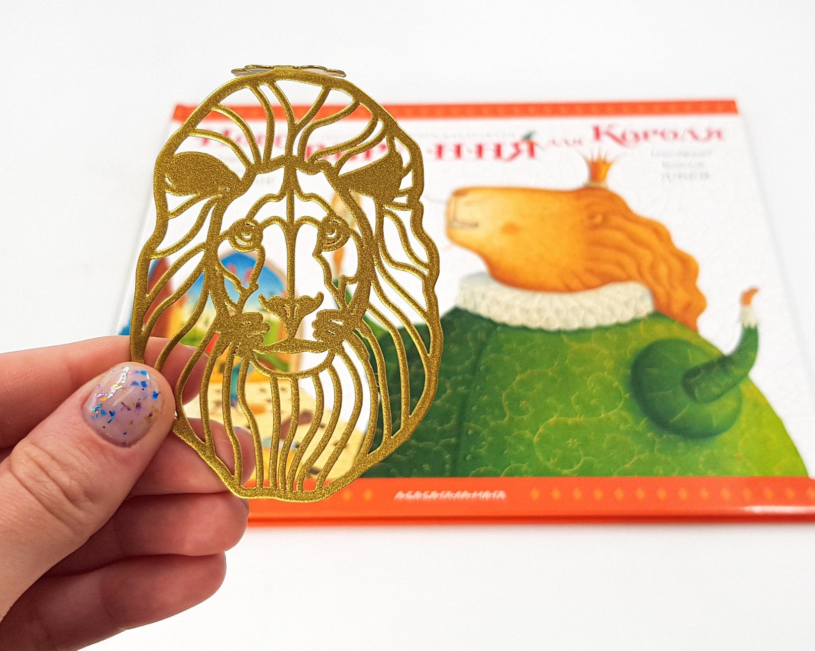 Lion Head metal bookmark in gold marking a page in an illustrated book, view 4