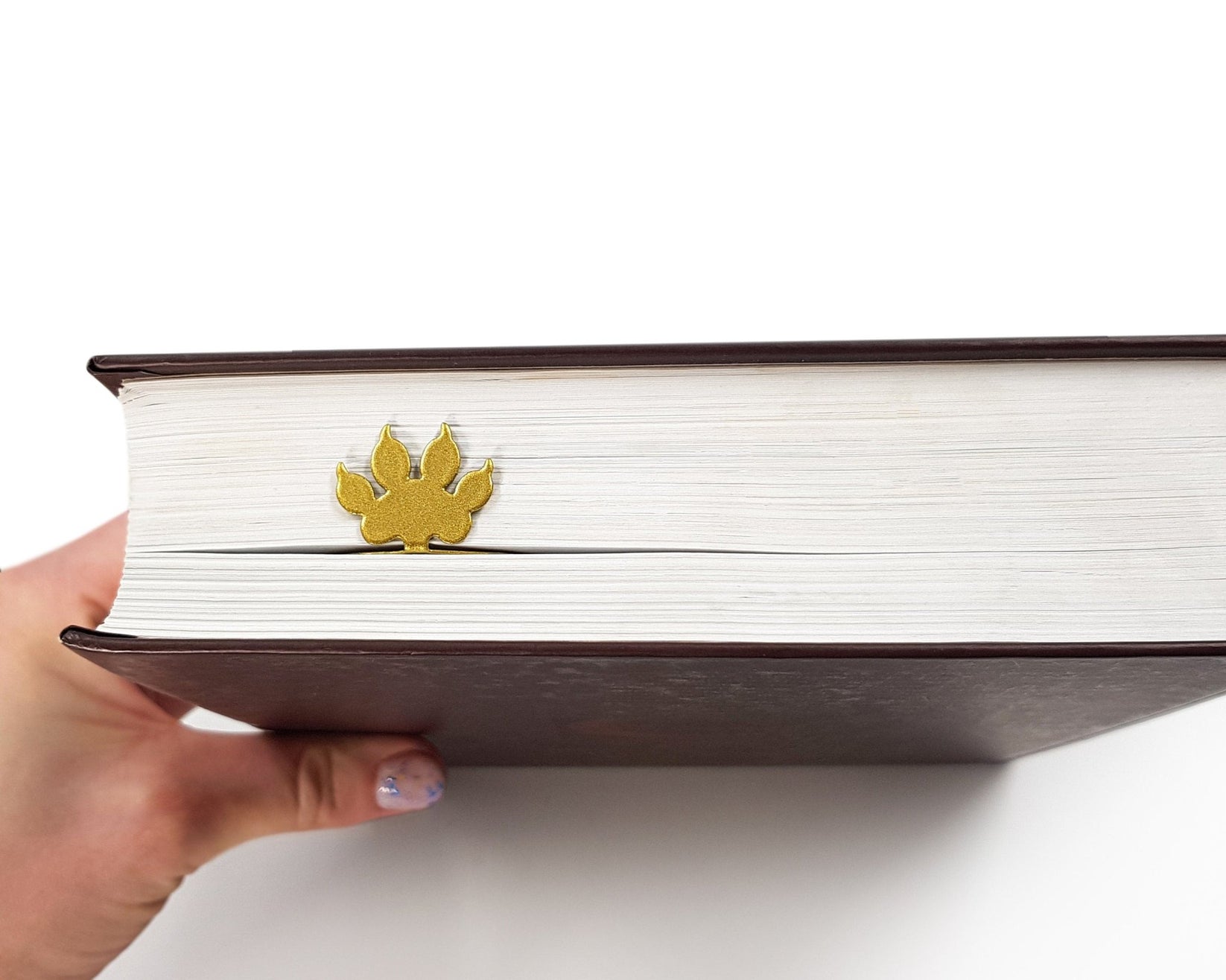 Lion Head metal bookmark in gold held up beside an open book