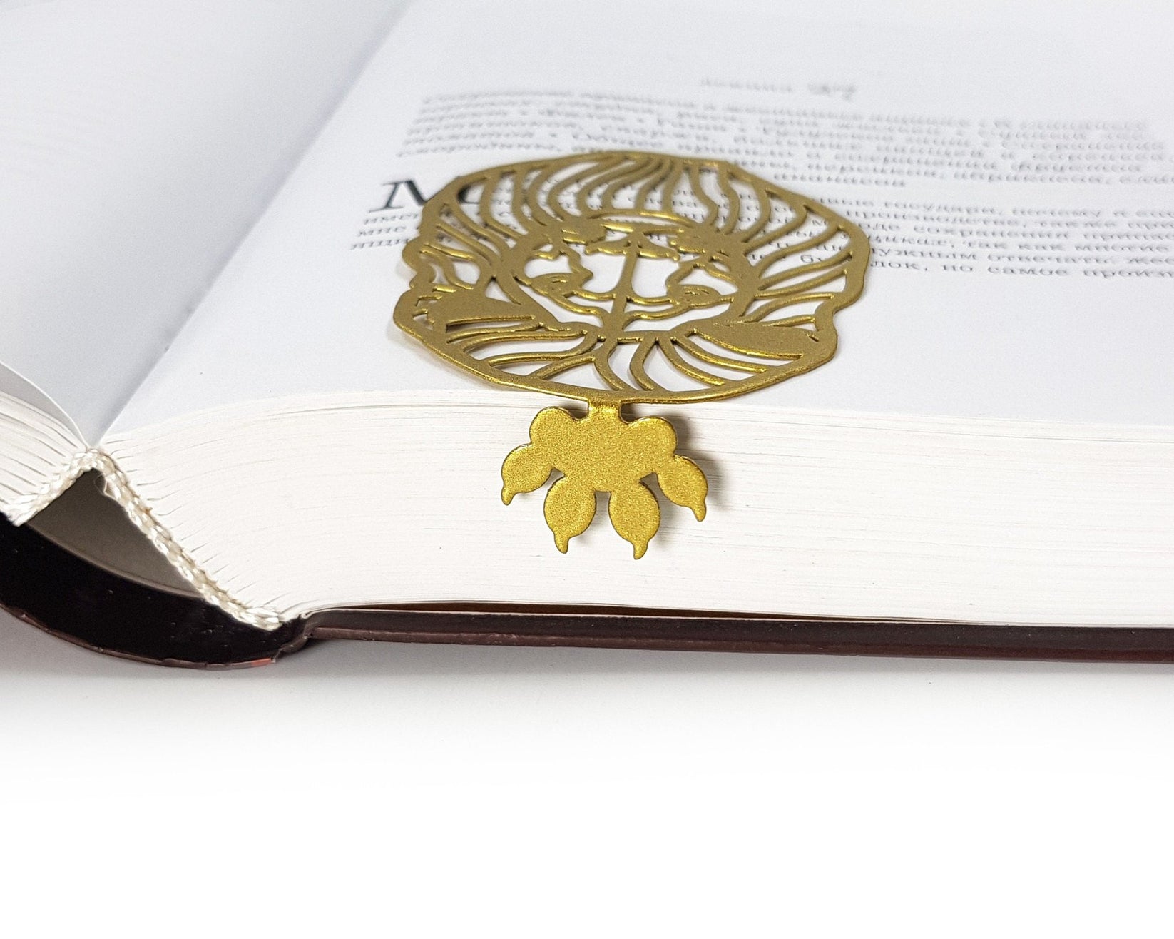 Lion Head metal bookmark in gold resting on the pages of an open book