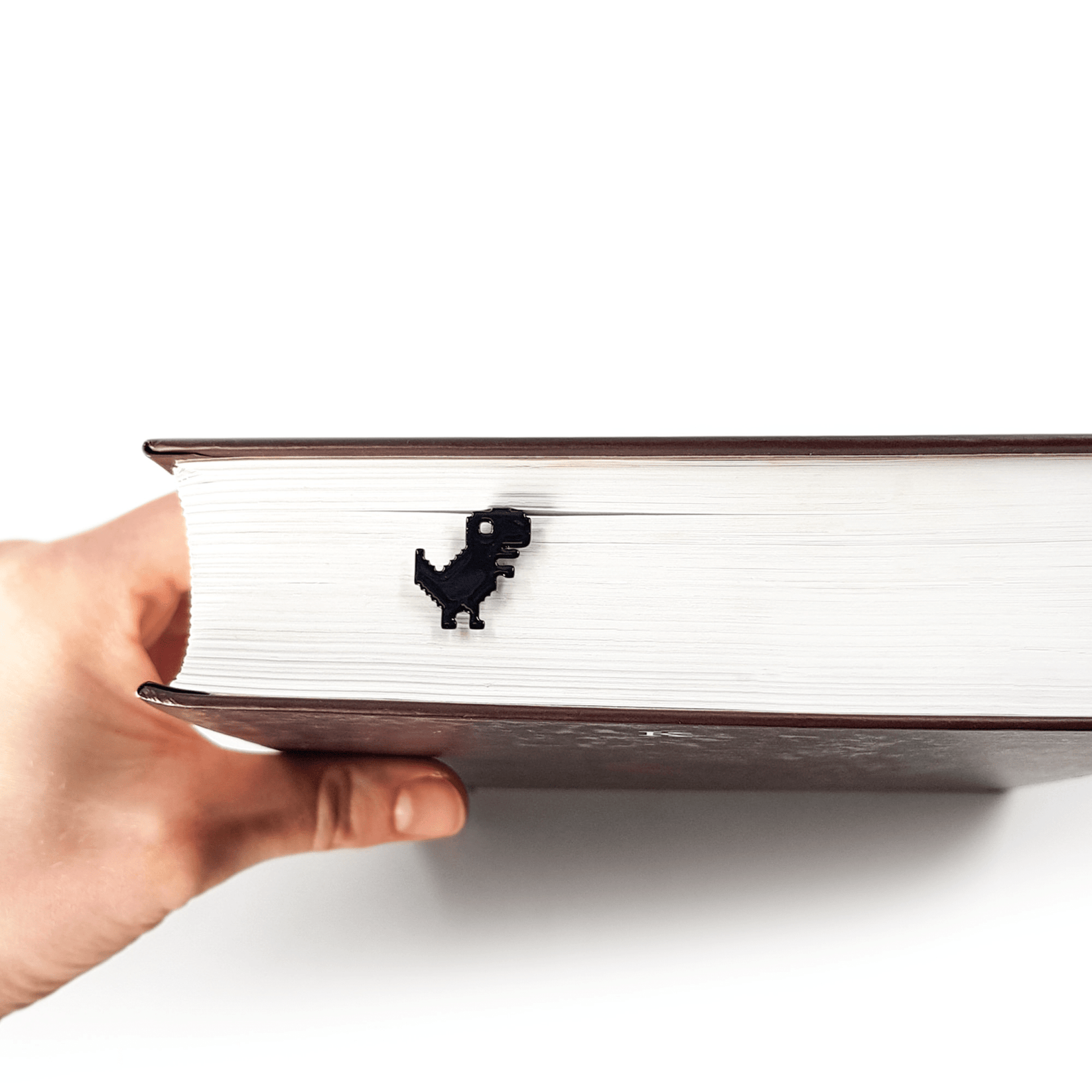 Little Dino metal bookmark held in a hand to show its size