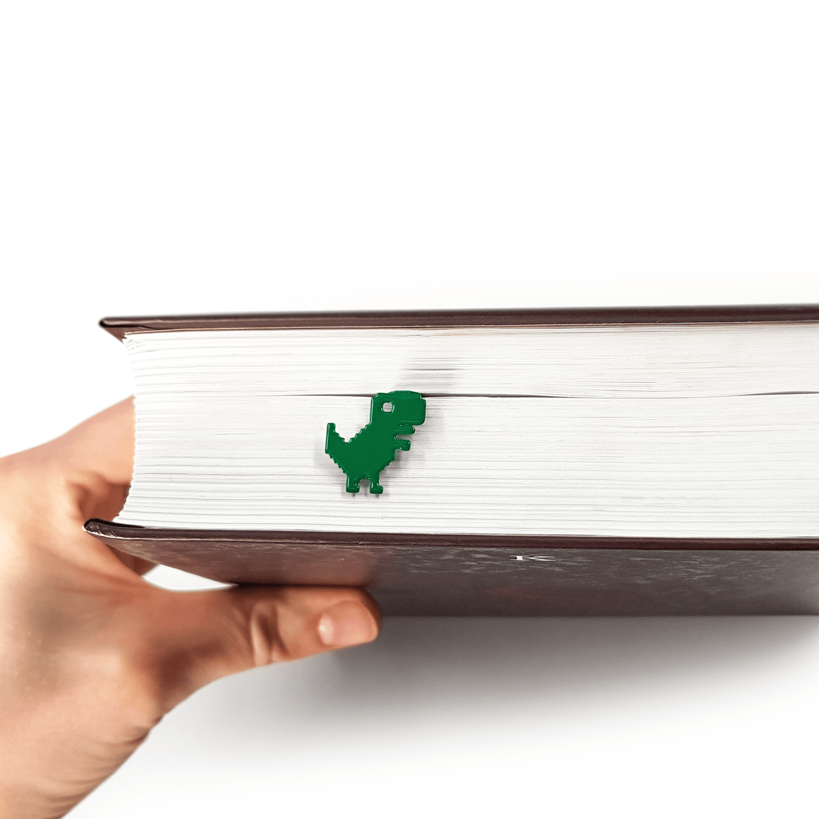 Little Dino metal bookmark in green held up beside an open book