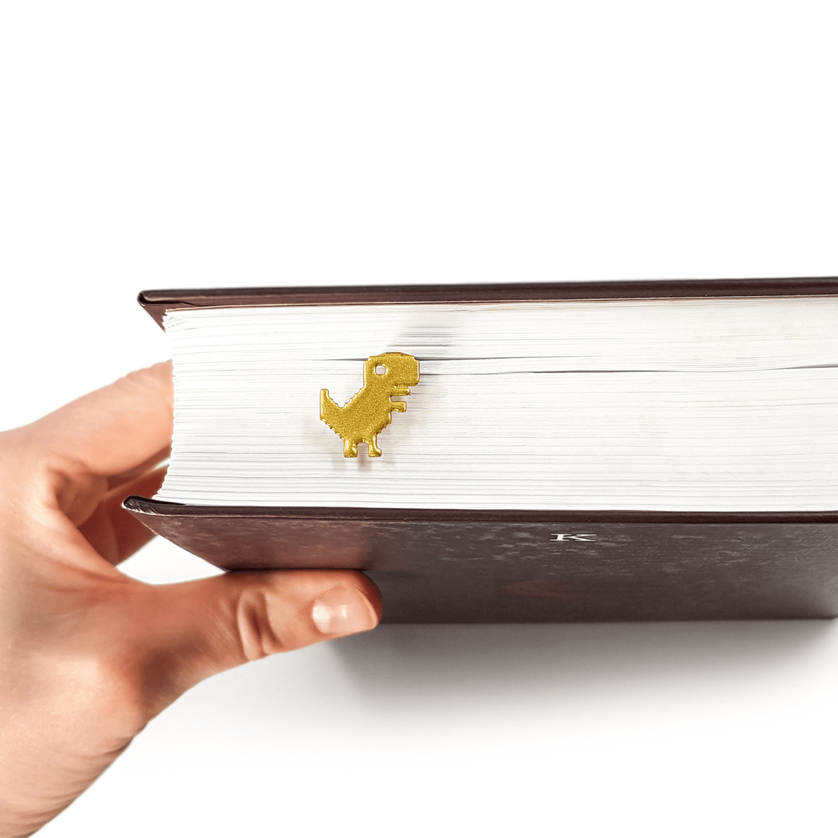 Little Dino metal bookmark in gold held in a hand above an open book