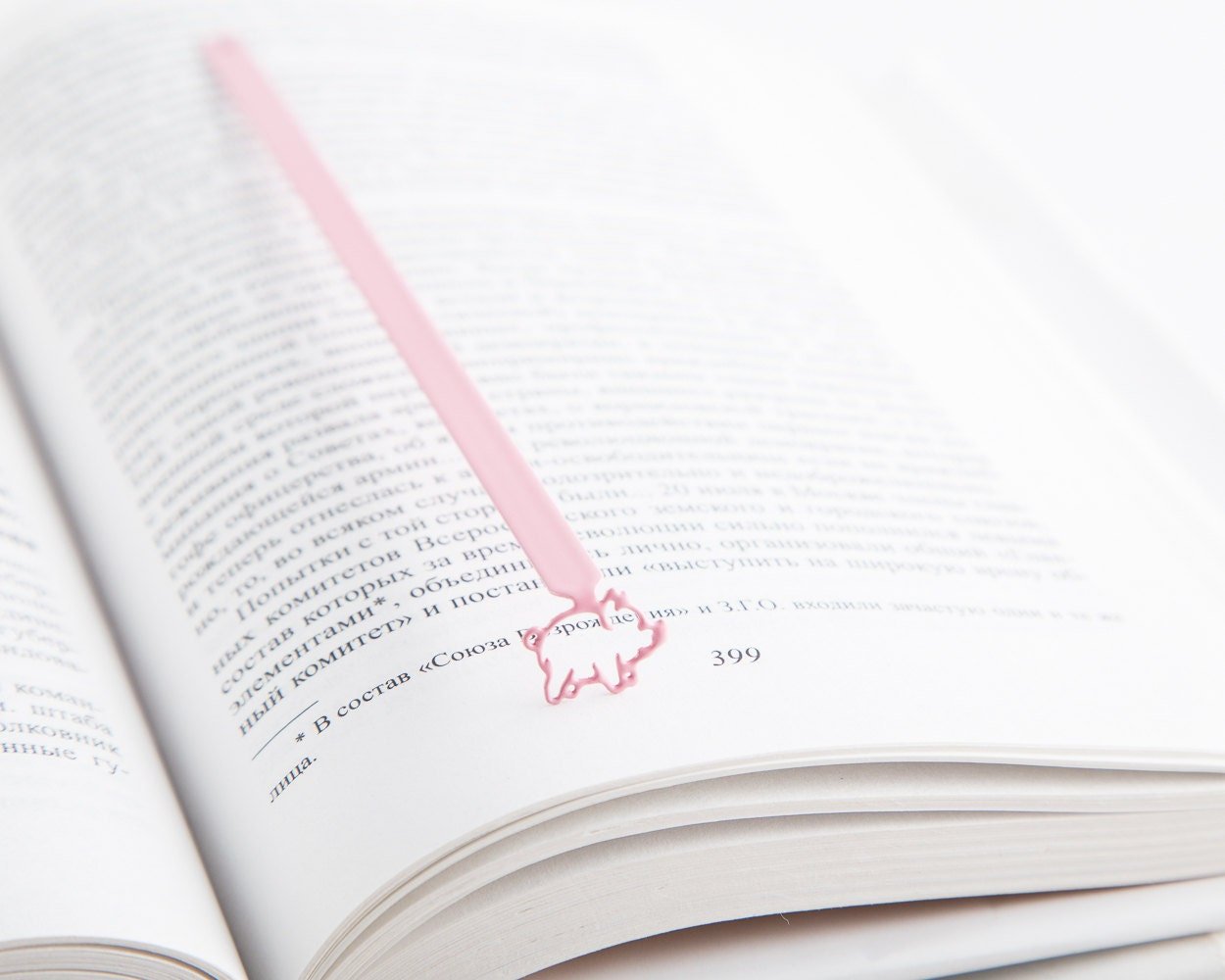 Little Piggy metal bookmark in red resting on the pages of an open book