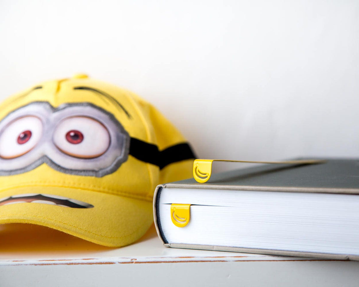 Many Bananas metal bookmark — yellow minion toy beside books with bookmark