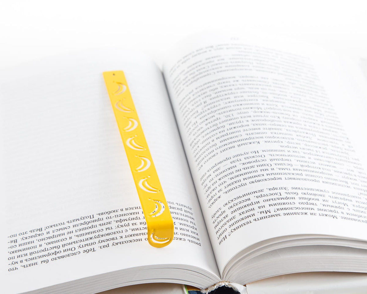 Many Bananas metal bookmark in gold resting on the pages of an open book