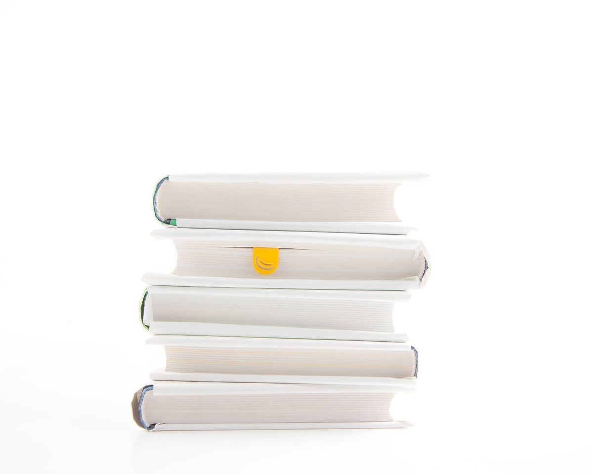 Many Bananas metal bookmark in gold shown with a stack of books