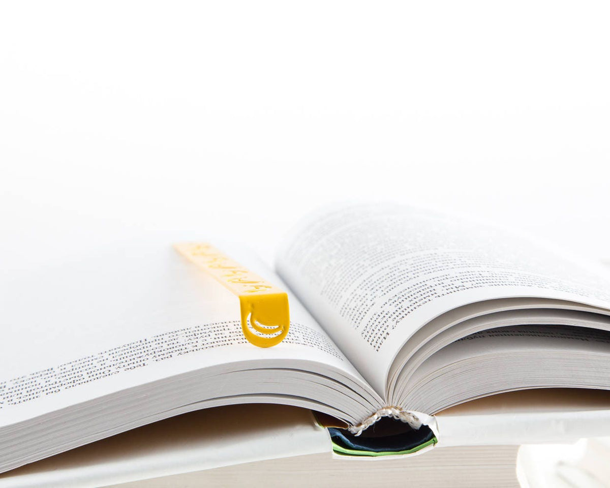 Many Bananas metal bookmark in gold lying across the pages of an open book