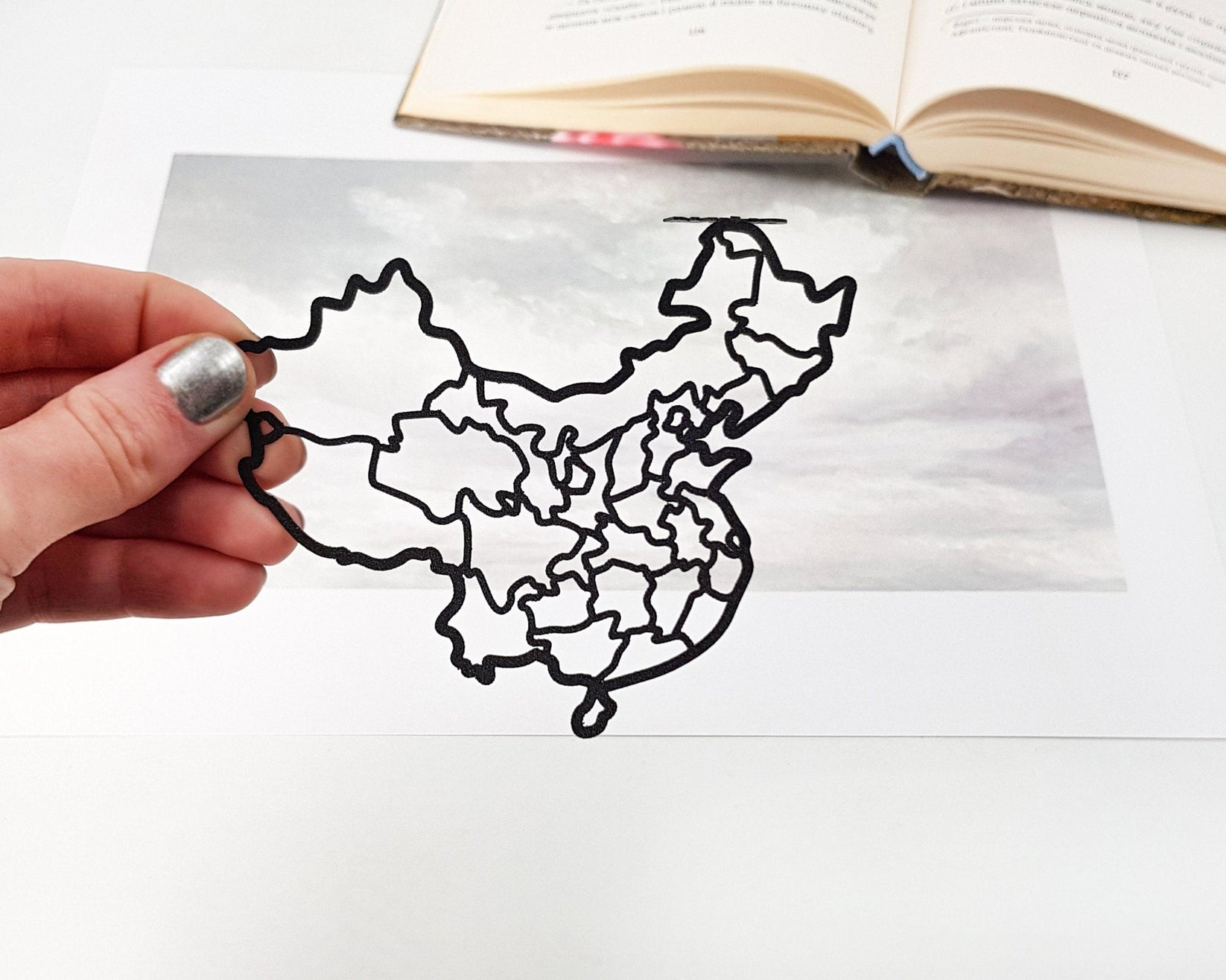 Map of China metal bookmark held in a hand above an open book